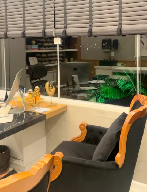 Recepção com balcão iluminado, persianas e poltronas de espera